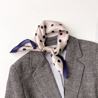 Champagne silk scarf with navy polka dots elegantly tied around collar of geometric pattern blazer, showcasing luxurious texture and versatile styling
