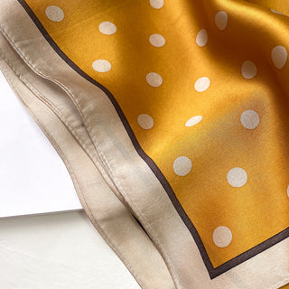 Mustard yellow silk scarf with white polka dots, featuring a champagne-colored border with brown trim, showcasing the luxurious texture and elegant design.