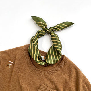 Moss green silk bandana with gold stripes tied stylishly around the collar of a camel brown sweater, showcasing its luxurious sheen and versatile wear style