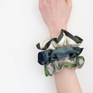 Set of three luxurious silk scrunchies on a wrist, featuring black and white, navy and teal, and khaki with green edge contrast designs