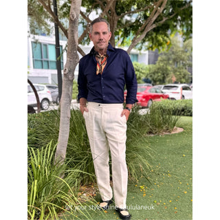 Man wearing a navy blue shirt and a luxury silk scarf with navy and beige paisley pattern featuring vibrant orange border, standing outdoors. 