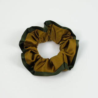 Luxurious silk scrunchie with copper-gold center and dark green edge trim, showcasing smooth silky texture and ruffled design