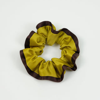 Luxurious silk scrunchie with mustard yellow fabric and contrasting brown edge trim, showcasing ruffled texture on white background