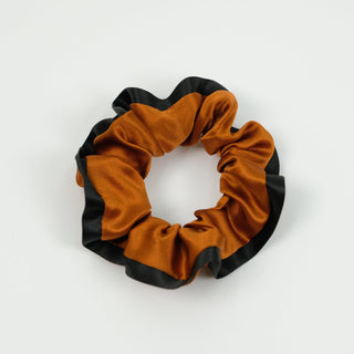 Luxurious silk scrunchie in copper orange with black contrasting edge, showcasing ruffled texture and shiny fabric against white background