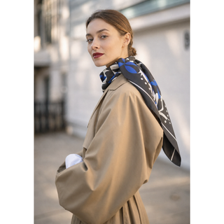 Woman wearing the English Seaside Pebble 90cm silk scarf in blue, black and ivory, styled over a camel coat.