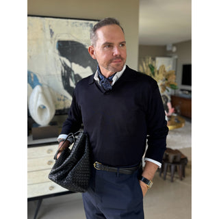 Man wearing a navy patterned silk square neckerchief by LuluLane in a dark navy sweater and trousers holding a black bag, showcasing a refined and sharp look.