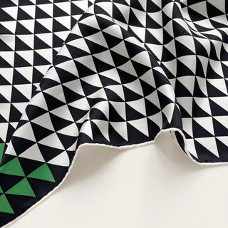 Close-up of a 53cm geometric silk bandana with black and white triangle pattern and green corner, hand-rolled hems.