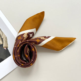 Amber taupe silk neckerchief with 70s-inspired geometric pattern, featuring burgundy, tan and cream colors with hand-rolled edges, displayed artfully coiled