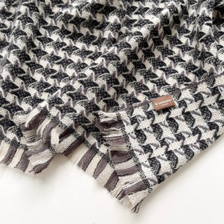 Close-up of a taupe, black and cream white cashmere scarf with houndstooth check pattern and LuluLane label