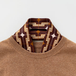 Retro 70s silk scarf in burgundy, amber and beige with geometric pattern, styled with a tan sweater, showcasing hand-rolled edges