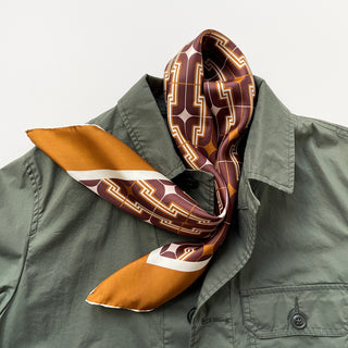 Vintage 70s silk neckerchief with burgundy, amber and beige geometric pattern, elegantly styled on olive green shirt collar