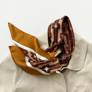 Vintage 70s silk neckerchief featuring geometric pattern in burgundy, amber and beige tones, elegantly displayed on beige collar