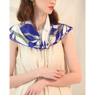 Woman wearing a blue iris patterned silk scarf in a cream dress