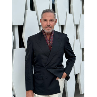 Man wearing burgundy paisley silk square scarf by LuluLane in a black blazer and white trousers with a white wall background