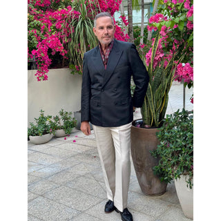 Man wearing burgundy paisley silk square scarf by LuluLane in a black blazer and white trousers standing outdoors with plants and flowers in the background