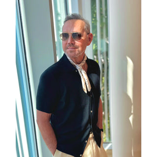 Man wearing an ivory paisley pattern silk bandana square by LuluLane in dark blazer and white trousers with sunglasses showcasing a refined, smart causal look.