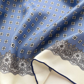 Close-up of cornflower blue silk scarf featuring vintage micro-motifs and lace-inspired border, 65cm square design with hand-rolled hems.