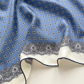 Close-up of cornflower blue silk scarf featuring vintage micro-motifs and lace-inspired border, 65cm square design with hand-rolled hems.