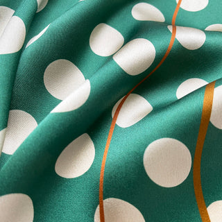 Close-up of a jade green silk bandana scarf with cream polka dots showing luxurious fabric texture.