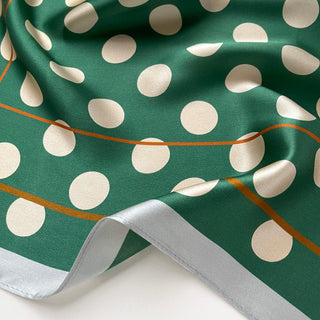 Close-up of a jade green silk bandana scarf with cream polka dots showing luxurious fabric texture.