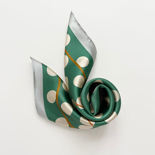 Jade green silk bandana scarf with cream polka dots and gold accents on a light grey background.