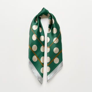 Jade green silk bandana scarf with cream polka dots, gold accent and light grey trim edge knotted elegantly on a light grey background.