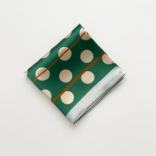 Folded jade green silk bandana scarf with cream polka dots and thin gold stripes on a light grey background.