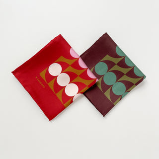 Two folded geometric mid-century silk scarf by LuluLane with Bauhaus-inspired design - one in red, pink and brown tones and the other in chocolate brown and teal green tones.
