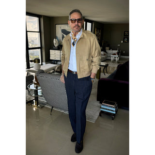 Man wearing unisex chess board pattern silk square scarf in golden squash yellow and navy by LuluLane in khaki racer jacket, white shirt and navy trousers showcasing a smart look.