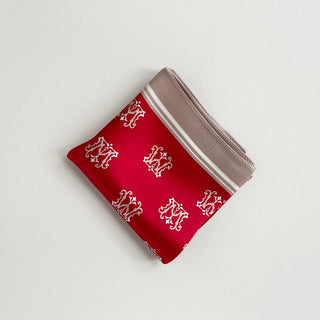 Red silk square scarf with white crown pattern and taupe border, folded into a triangle showing elegant royal design