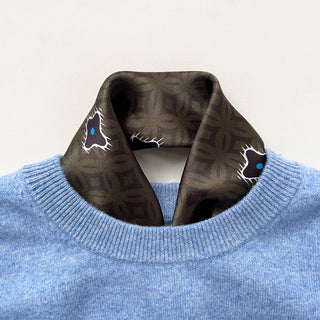Olive green silk neckerchief with geometric star pattern and blue accents, styled with light blue sweater, displaying luxurious texture and versatile wear.
