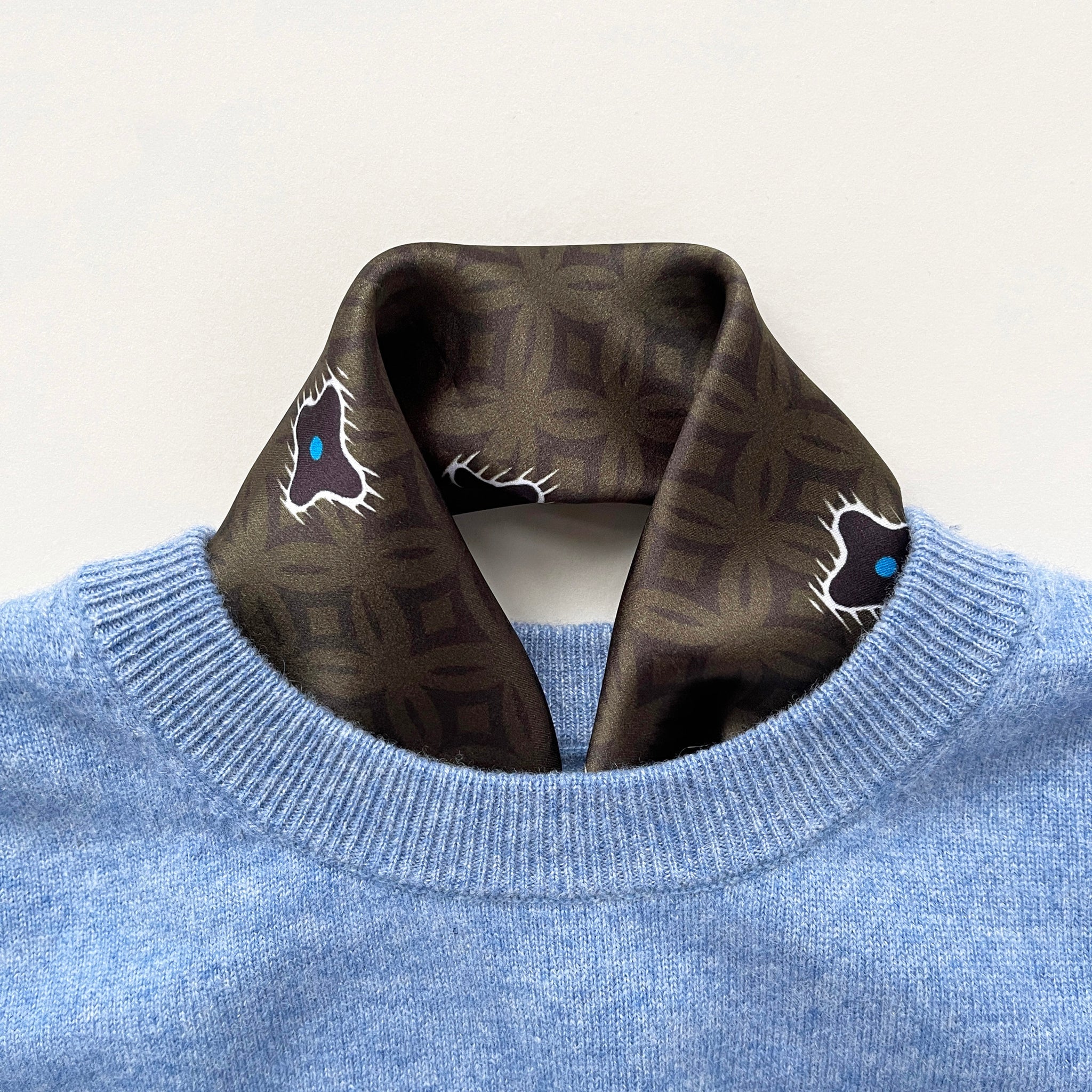 a dark olive green silk scarf neckerchief featuring timeless print, tucked in a sky blue men's sweater