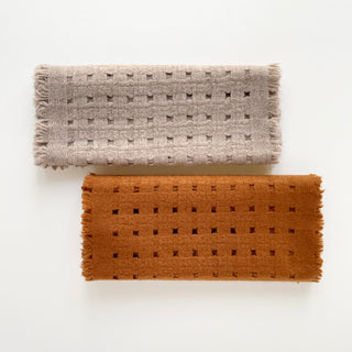 Two pure cashmere scarves featuring openwork jacquard design in mustard brown and beige on a light grey background.