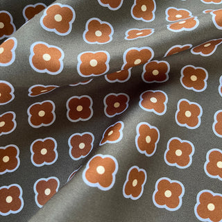 Close-up of a lead grey silk square scarf by LuluLane with rust red four-petal flower motif, double-sided print and hand-rolled hems.