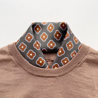 Lead grey silk square scarf by LuluLane with rust red four-petal flower motif tucked into a brown sweater as a polished neckwear for men.