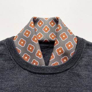 Lead grey silk square scarf by LuluLane with rust red four-petal flower motif tucked into a dark grey sweater as a polished neckwear for men.