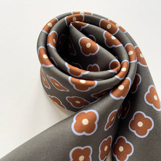 Close-up of a lead grey silk square scarf by LuluLane with rust red four-petal flower motif.