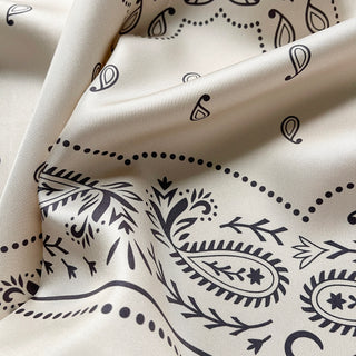 Close-up an ivory silk bandana scarf, 65cm square with modern paisley design and hand-rolled hems by LuluLane.