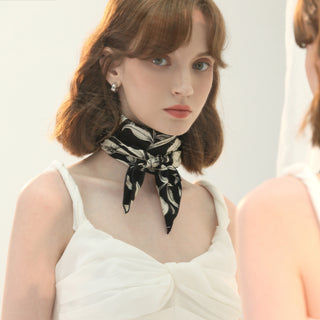 Women’s black and white floral silk scarf tied at neck, elegant monochrome styling with sleeveless white top.