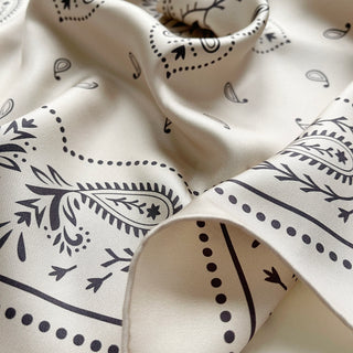 Close-up an ivory silk bandana scarf, 65cm square with modern paisley design and hand-rolled hems by LuluLane.
