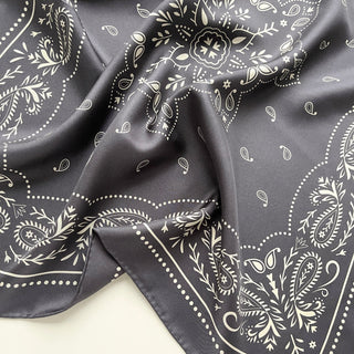 Close-up of a unisex charcoal grey silk bandana scarf, 65cm square with modern paisley print and hand-rolled hems by LuluLane.
