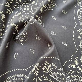 Close-up of a unisex charcoal grey silk bandana scarf, 65cm square with modern paisley print and hand-rolled hems by LuluLane.