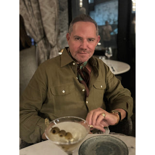 Man wearing Retro Bauhaus silk bandana square scarf in teal green and chocolate brown by LuluLane in a olive green jacket style shirt sitting at a table with a cocktail in a bar setting.