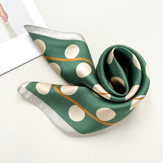Jade green silk square scarf with beige polka dots and gold stripe accents, elegantly draped to showcase its lustrous fabric and silver trim