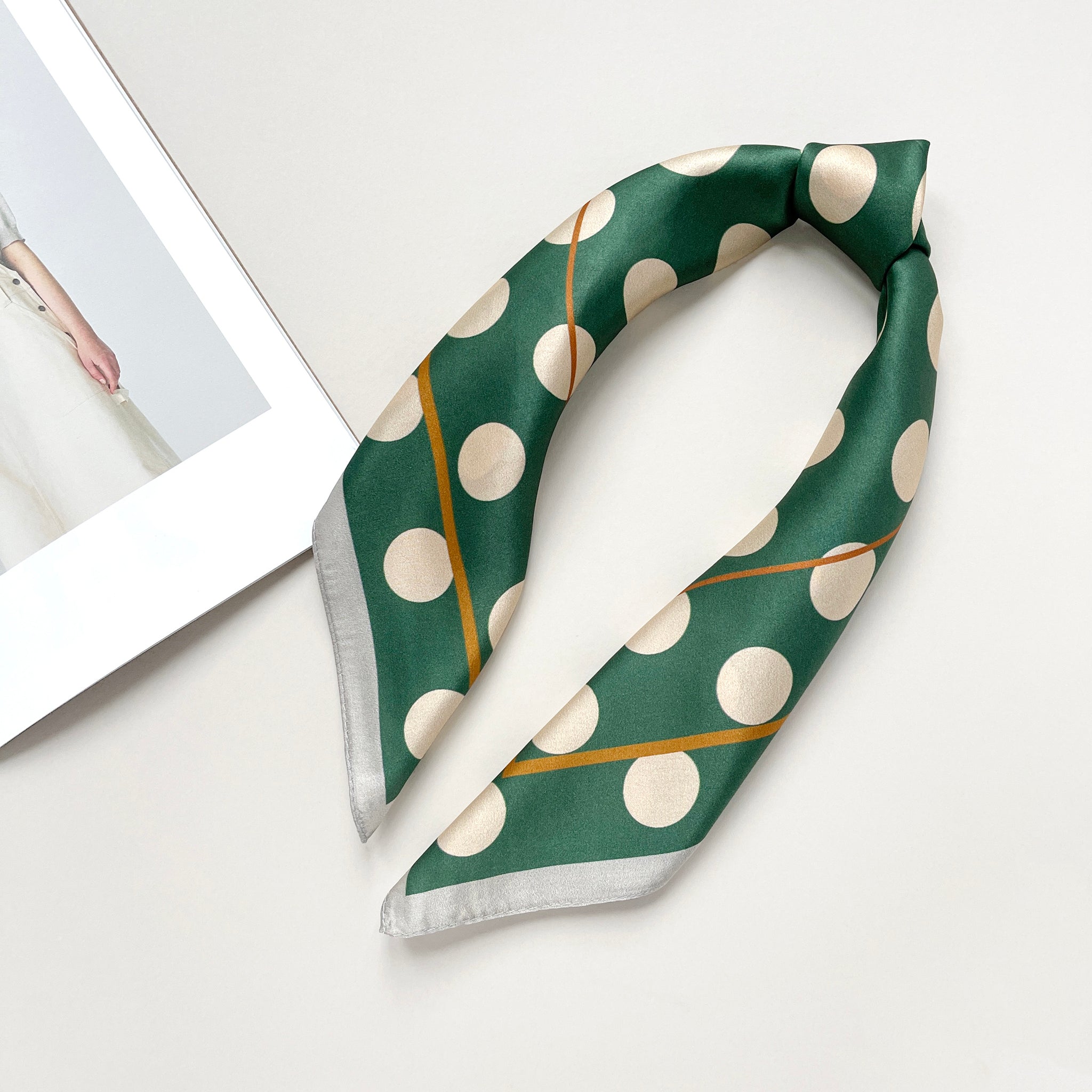 a jade green silk scarf bandana featuring light beige polka dot print, knotted as a headband 