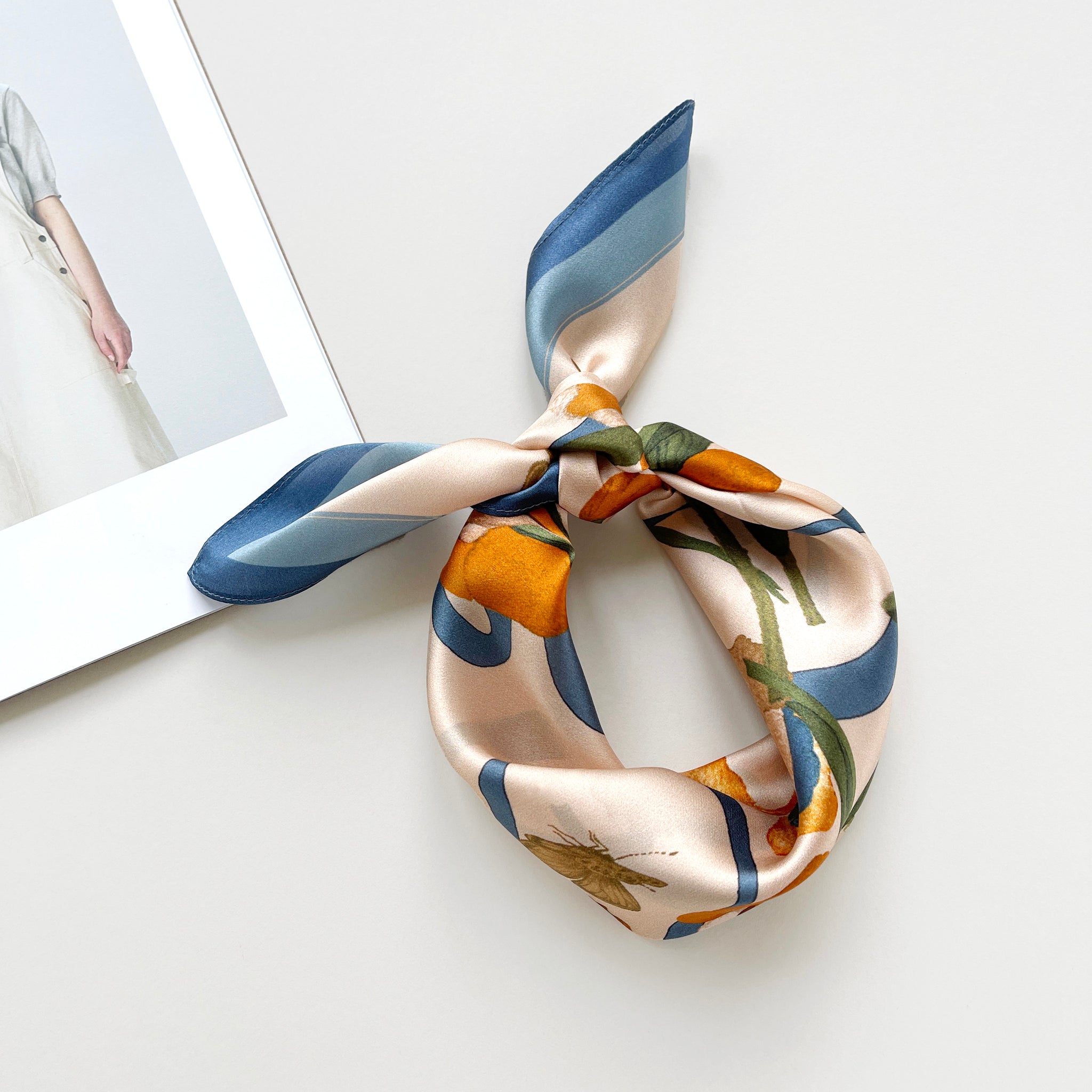 a small silk scarf in sky blue and orange  featuring lily and butterfly prints knotted as a headband