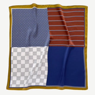 Navy geometric silk neckerchief featuring four distinct quadrants with checkerboard, solid blue, striped rust, and dotted blue patterns, bordered by gold trim.