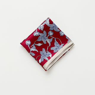 Folded women's silk bandana scarf by LuluLane with vibrant red background featuring blue floral botanical pattern and cream-colored border.