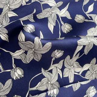 Close-up of a women's silk bandana scarf by LuluLane with deep navy blue background featuring elegant white floral pattern.
