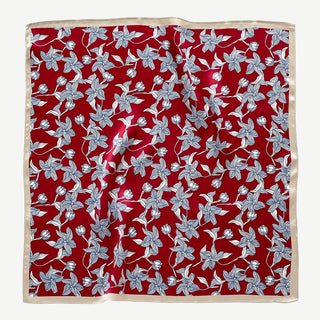 Square silk bandana scarf by LuluLane with vibrant red background featuring blue floral botanical pattern and cream-colored border, displayed flat.